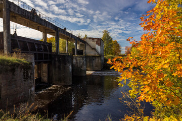 Fototapeta premium Autumn landscape at the old abandoned hydroelectric power station built on a small river in the Pskov region. The legacy of the past economic growth of the Soviet Union