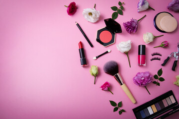 makeup cosmetics and equipment with flowers on pink background with copy space. top view