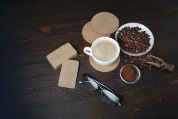 Still life with coffee cup, coffee beans, ground powder, beer coasters, blank kraft business cards and glasses on wooden background. Top view. Flat lay.