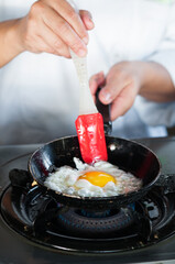 Closeup of a chef frying an egg on small pan.
