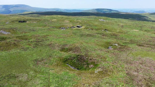 Aerial view revealing the entrance to a cave on remote moorland with background mountains (Chartist Cave, Wales, UK)