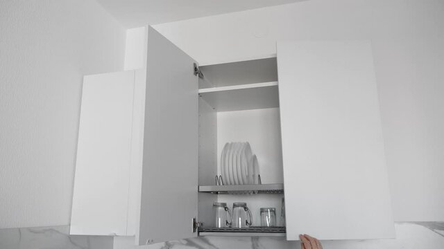 Female hand open kitchenware drying rack with plates and cups in white kitchen cabinet