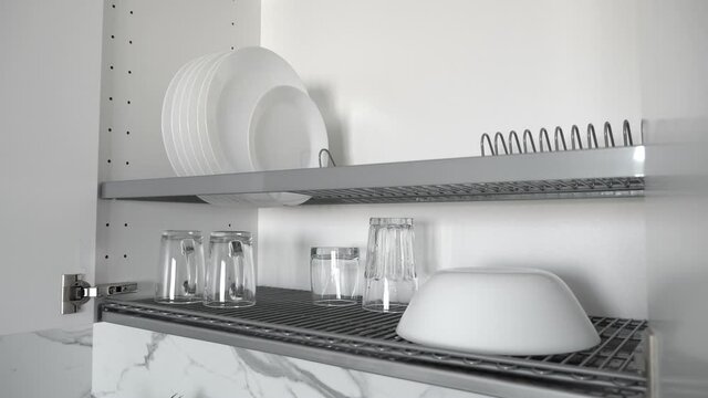 Kitchenware drying rack with plates and cups in white kitchen cabinet. Nobody