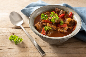 Fresh cooked goulash or stew from beef, onions and red bell pepper with parsley garnish in a bowl...
