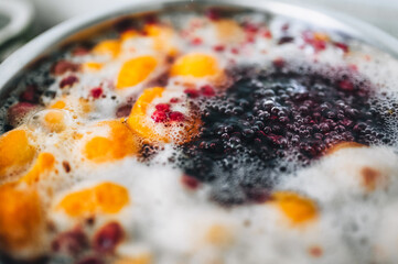 Fresh fruits are boiled in boiling water in a metal pan on a stove with bubbles and foam close-up. Cooking a delicious compote of apricot, apples, cherries, raspberries. Photography, concept.