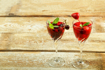Crystal glass with cherry juice and strawberry and fresh berries and mint inside on a wooden table. Copy space.