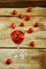 Crystal glass with strawberry and fresh berries and mint inside on a wooden table and berries on the table.
