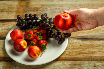 Female hand takes peach from fruit plate.