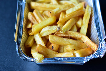 Delicious French fries in an aluminum container on a black background