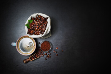 Fresh delicious coffee. Coffee cup and coffee beans in canvas bag and ground powder on black wooden background. Lot of copy space for your text. Flat lay.
