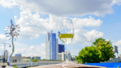 Glass of white wine with reflection on the blurred cityscape and dramatic sky background. Space for text. Wine concept.