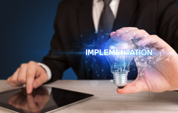 Businessman holding light bulb with IMPLEMENTATION inscription, innovative technology concept
