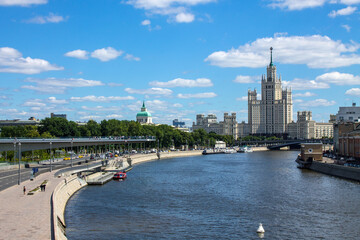 Fototapeta na wymiar Panoramic view of the house on Kotelnicheskaya embankment and the Moscow river with pleasure boats on a clear summer day with blue sky and white clouds and copy space