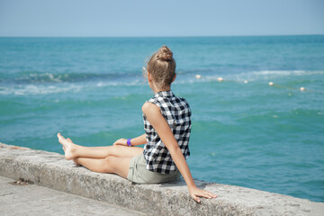 The girl is sitting with her legs stretched out on the breakwater