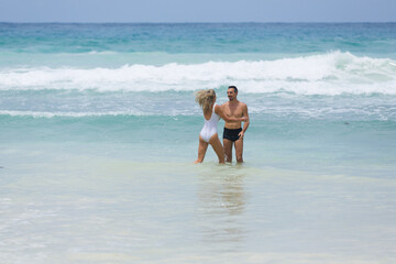 Long haired blonde woman in white swimsuit plays with her husband enjoining their honeymoon vacation at tropical beach together.