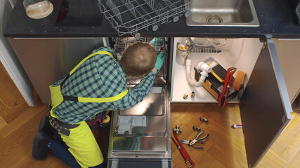 Fototapeta premium Young Caucasian Repairman Fixing Dishwasher In Kitchen