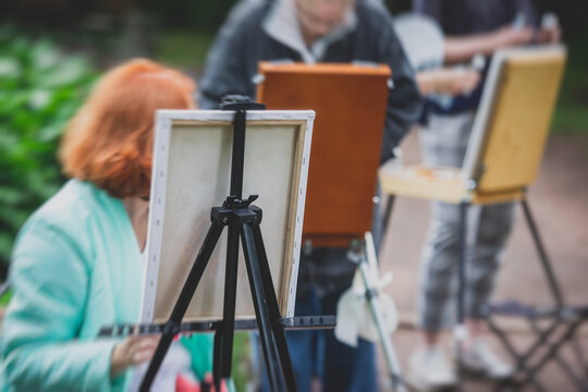 Process of plein air painting, group class of adult talented students in the park with paints easels, and canvases during lesson of watercolour painting outdoors