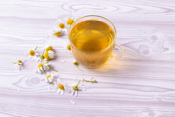 herbal fresh hot tea in a glass cup and camomile flowers