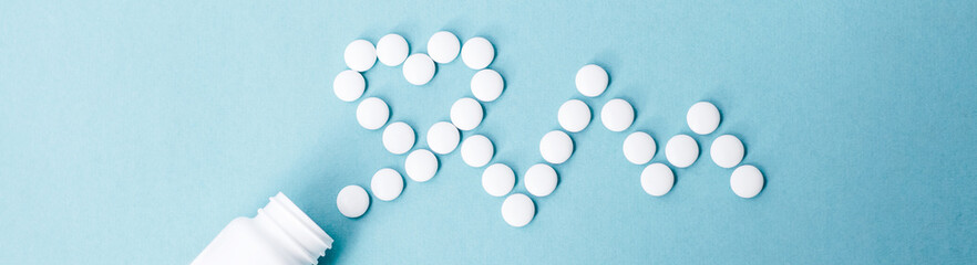 Top view of heart and cardiogram made of white pills over blue background. Heart and cardiovascular disease, health and treatment concept. Horizontal shot