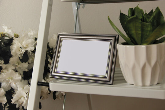 The Mockup Of The Metallic Photo Frame And Flower Pot Stand On The Shelf.