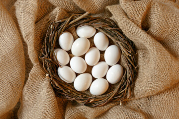White chicken eggs wrapped in burlap next to a basket on a White eggs on burlap background