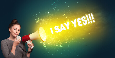 Young woman yelling to loudspeaker with I SAY YES!!! inscription, modern media concept