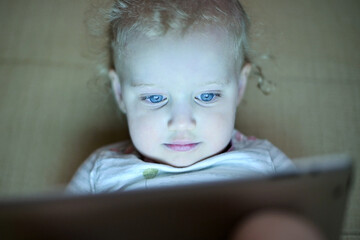 The little girl is fascinated by the screen of the tablet. The child is watching cartoons, front...
