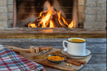Golden latte milk made with turmeric and spices before cozy fireplace. Healthy drink.