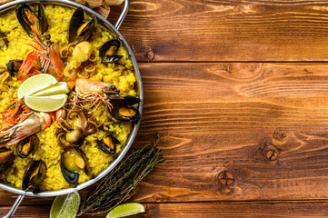 The Spanish paella with seafood prawns, shrimps, mussels in a paellera.  Wooden background. Top view. Copy space