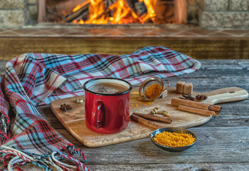 Golden latte milk in red mug with turmeric and spices before cozy fireplace. Healthy drink.