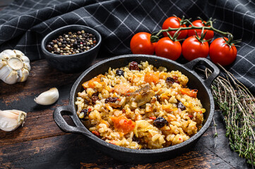 Rice pilaf with lamb meat and vegetables in a pan.  Dark wooden background. Top view