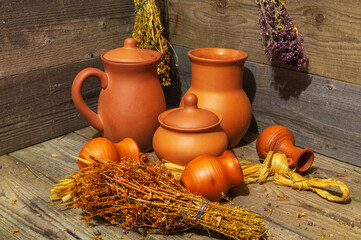 Still life with clay jugs of various sizes and bundles of dried medicinal herbs on wooden table.