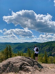 Top view. A young man stands on top of a mountain and enjoys panoramic views of mountains and forests.
