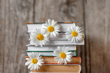 Stacked books on top of each other with daisies between the pages on a wooden background.