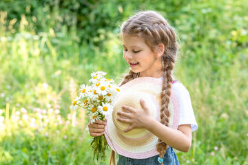A beautiful little girl admires a bouquet of wild flowers in a green clearing.