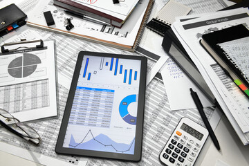 business office desk closeup - tablet computer with tables and graphs on the screen, financial reports, analysis and accounting, set of documents for bookkeeping