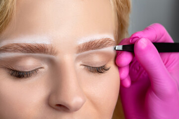 Woman having Permanent Make-up Tattoo on her Eyebrows. Eyelash artist plucks eyebrows with...
