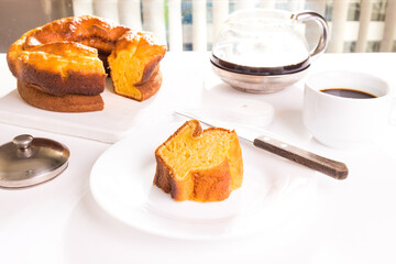 Pedaço de bolo de milho sobre o prato branco com o bolo cortado ao fundo junto com bule de café e xícara cheia