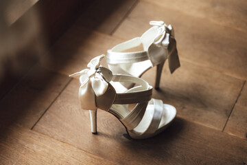 Side view of pair of white wedding shoes standing on wooden floor. Shoes are oriented in against each other. Wedding day concept.