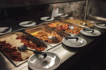 Row of stainless hotel pans on food warmers with various meals. Self-service buffet table....