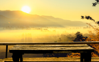 Old wooden table at the coffee shop blurred background  The sun's rays through at the top of the hill and the moving fog over the tree in the rice fields, Chiang Rai Northern  Thailand