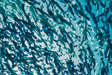 The texture of hanging blue and teal ribbons and tapes on the street on a bright day, they overlap each other, sway in the wind, and forming turbulent patterns, blue sky with sun flares behind