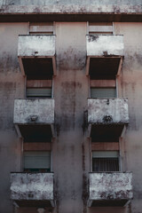 Vertical shot with a facade of a residential building: six balconies with single windows on each, some of them with partly closed blinds, a grungy wall with a blackened plaster, Lisbon, Portugal