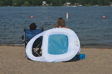 Lakeside Park, Big Lake, MN, USA - July 3, 2020. Two people sit on the beach looking at the water...