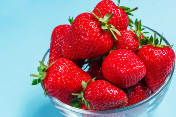 Many berries of ripe delicious strawberries lie in a glass bowl on a blue background. Background with strawberries. Summer berries. Healthy eating.