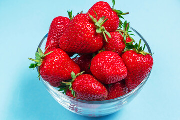Many berries of ripe delicious strawberries lie in a glass bowl on a blue background. Background with strawberries. Summer berries. Healthy eating.