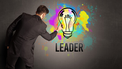 businessman drawing colorful light bulb with LEADER inscription on textured concrete wall, new business idea concept