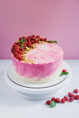 Celebratory cake with pink cream on a pink background. Cake decor made from fresh raspberries, crushed pistachios and mint. Green fresh mint leaves. Cake with raspberries. 