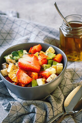 Fresh fruit salad in bowl with mint syrop on grey background