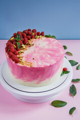 Celebratory cake with pink cream on a pink and blue background. Cake decor made from fresh raspberries, crushed pistachios and mint. Green fresh mint leaves. Cake with raspberries. 